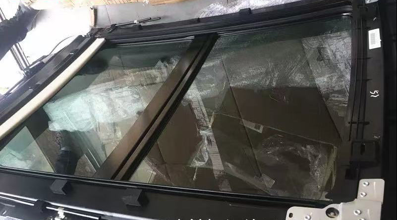 A black car sunroof window frame with a large glass panel, shown in a warehouse setting with cardboard boxes and protective plastic wrapping visible in the background. Chinese text overlays are present in the top left and bottom right.
