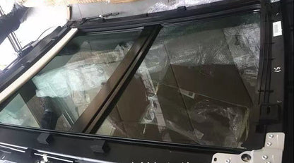 A black car sunroof window frame with a large glass panel, shown in a warehouse setting with cardboard boxes and protective plastic wrapping visible in the background. Chinese text overlays are present in the top left and bottom right.